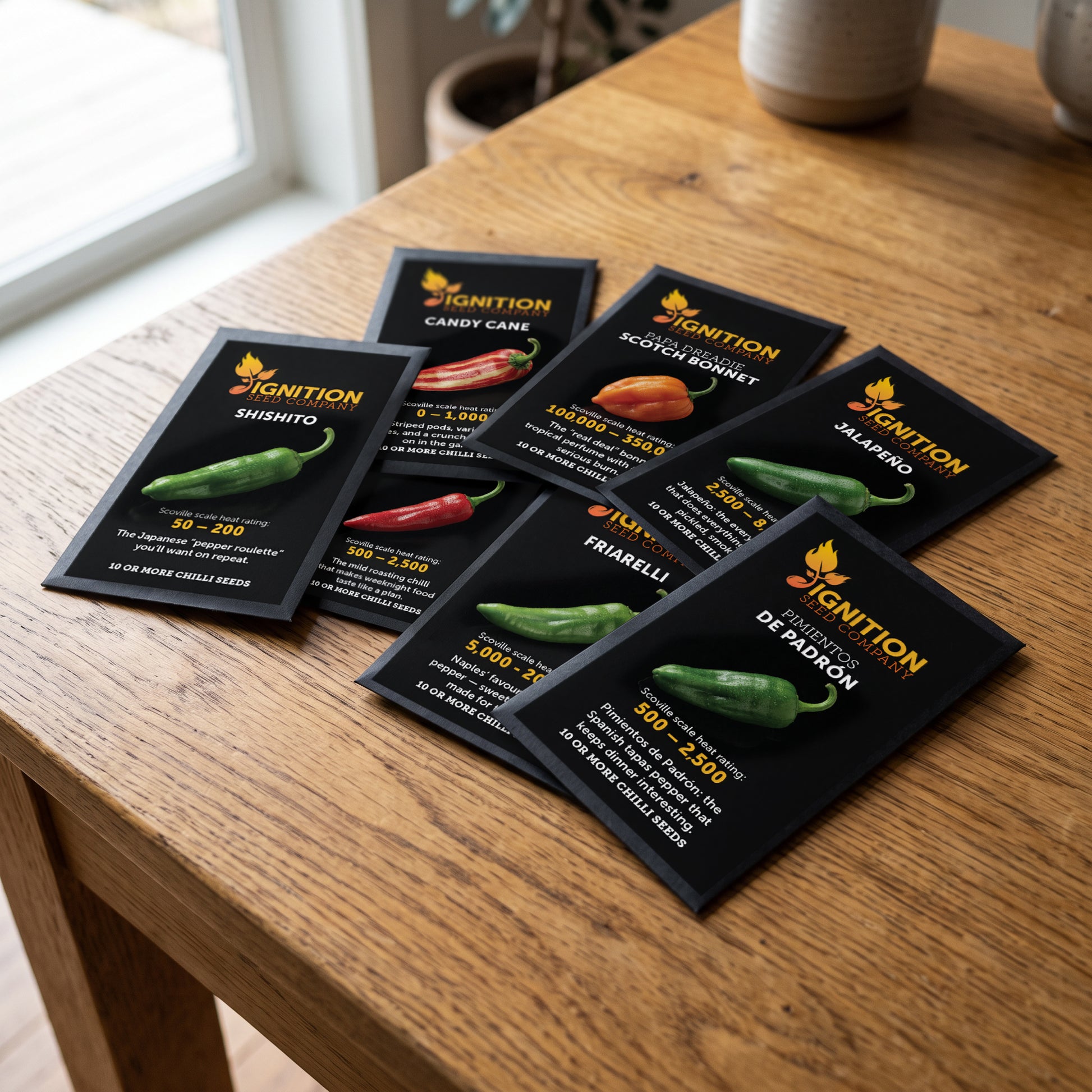 Seven black Ignition Seeds chilli seed packets spread across a wooden table