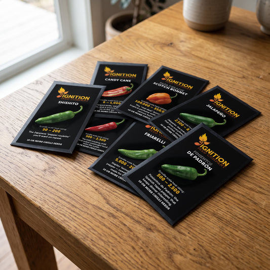 Seven black Ignition Seeds chilli seed packets spread across a wooden table